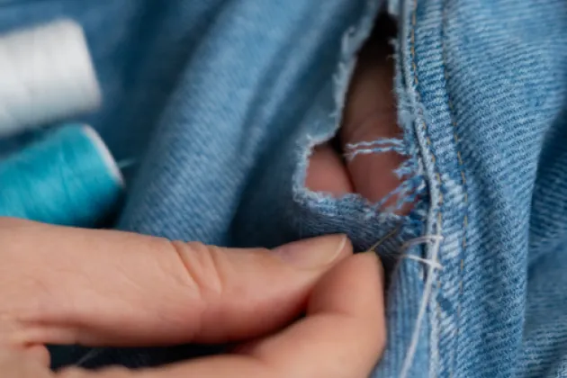 Image of denim jeans being repaired with sewing needle