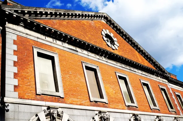 Exterior view of the Iveagh Markets showing the red brick façade, stone detailing and upper‑level windows beneath the pitched roof.