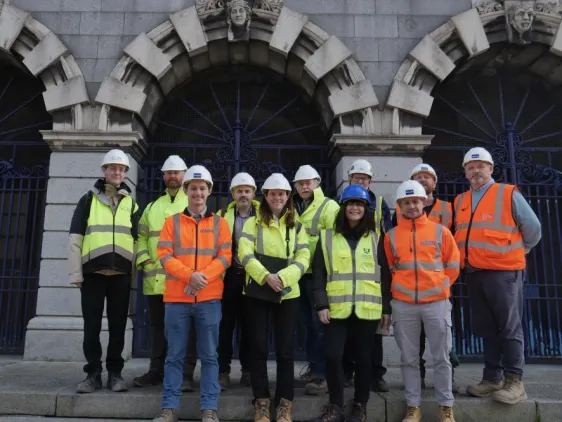 Group of people wearing high‑visibility clothing and safety helmets standing outside the Iveagh Markets during site works.