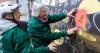 two women spray paint a bee on the wall