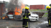 Fire fighter spraying down a training car that is on fire 