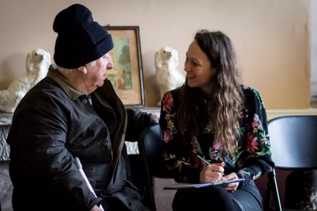 Older man and younger woman chatting. The woman is making notes with a pen and paper.