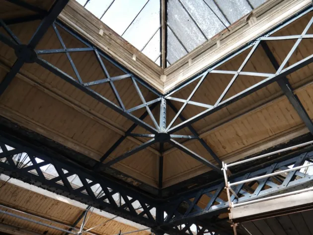 Detail view of intersecting metal roof trusses and glazed roof panels inside the Iveagh Markets, showing the original structural framework.