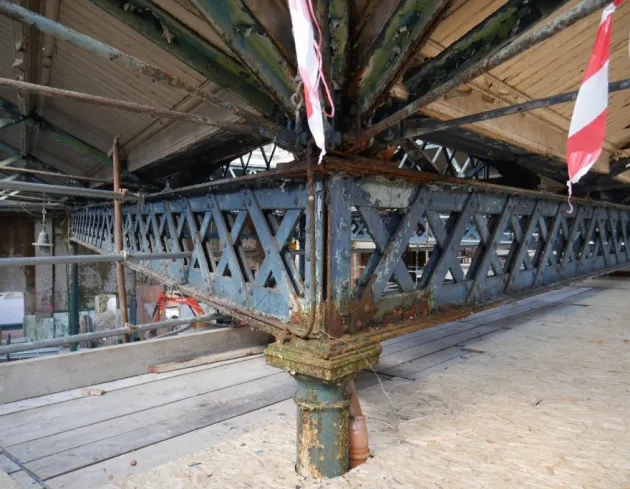 Close‑up of a cast iron column and lattice truss supporting the Iveagh Markets roof, showing corrosion and temporary supports during stabilisation works.