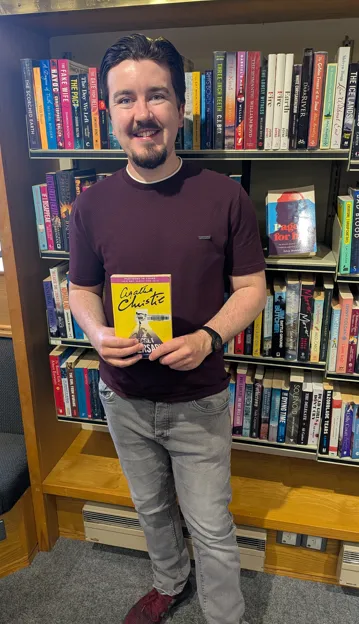 A member of staff holding the Agatha Christie novel The Secret Adversary